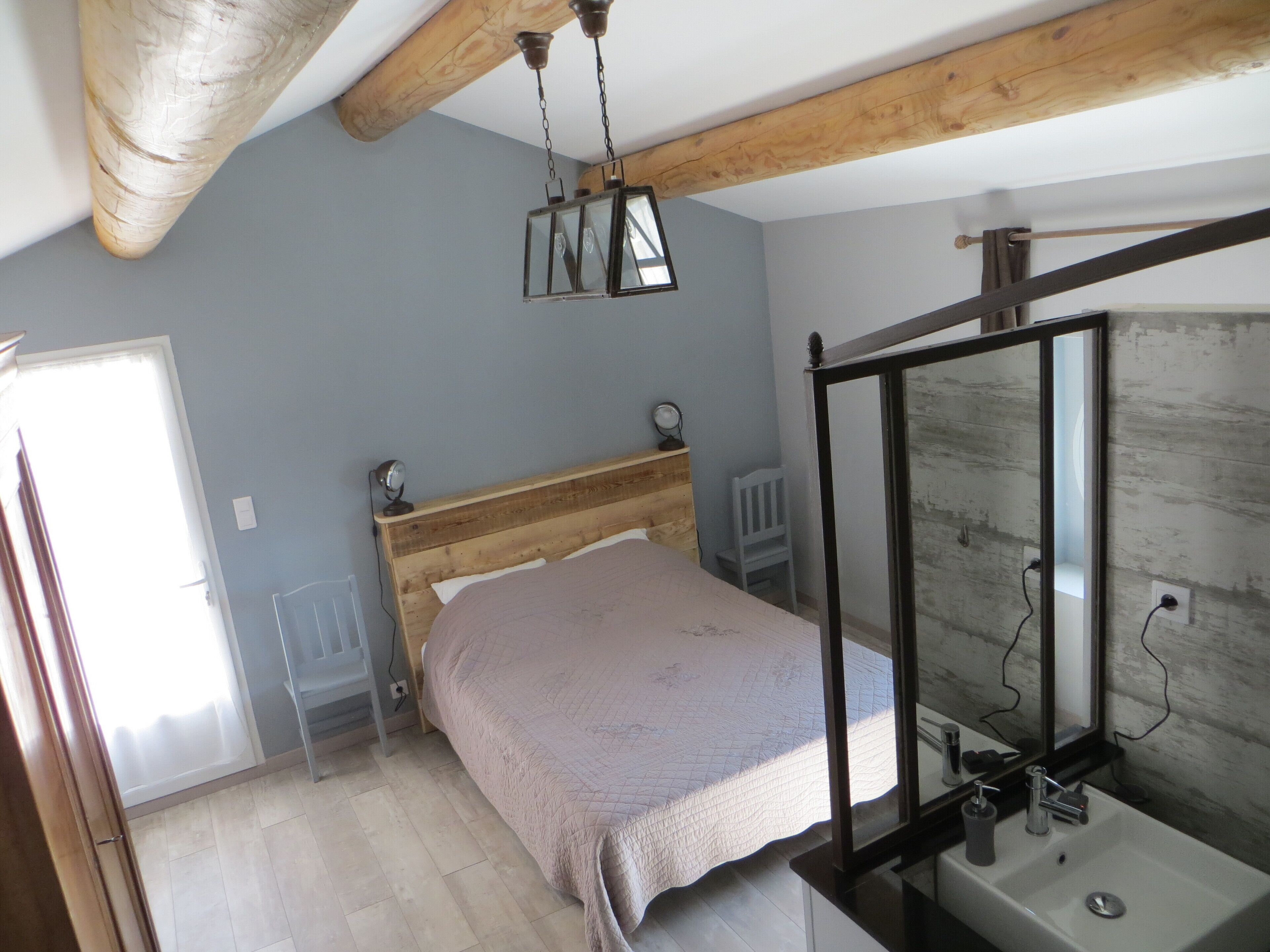 A bedroom with a wooden bed, a bedside table with a lamp, a mirror, and a window.
