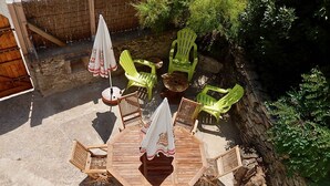 Un patio al aire libre con una mesa y sillas de madera, rodeado de sillas y sombrillas de plástico verde.