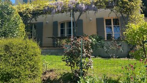 A two-story house with a tiled roof, multiple windows with shutters, and a garden with various plants and flowers. - Beautiful house with private heated infinity pool 16 km from Uzes (Connaux)