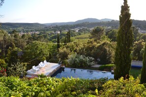 A pool with a deck, surrounded by lush greenery and tall trees. - Beautiful house with private heated infinity pool 16 km from Uzes (Connaux)