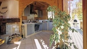 Interior rústico de una cabaña con chimenea de piedra, techo de madera y zona de cocina.