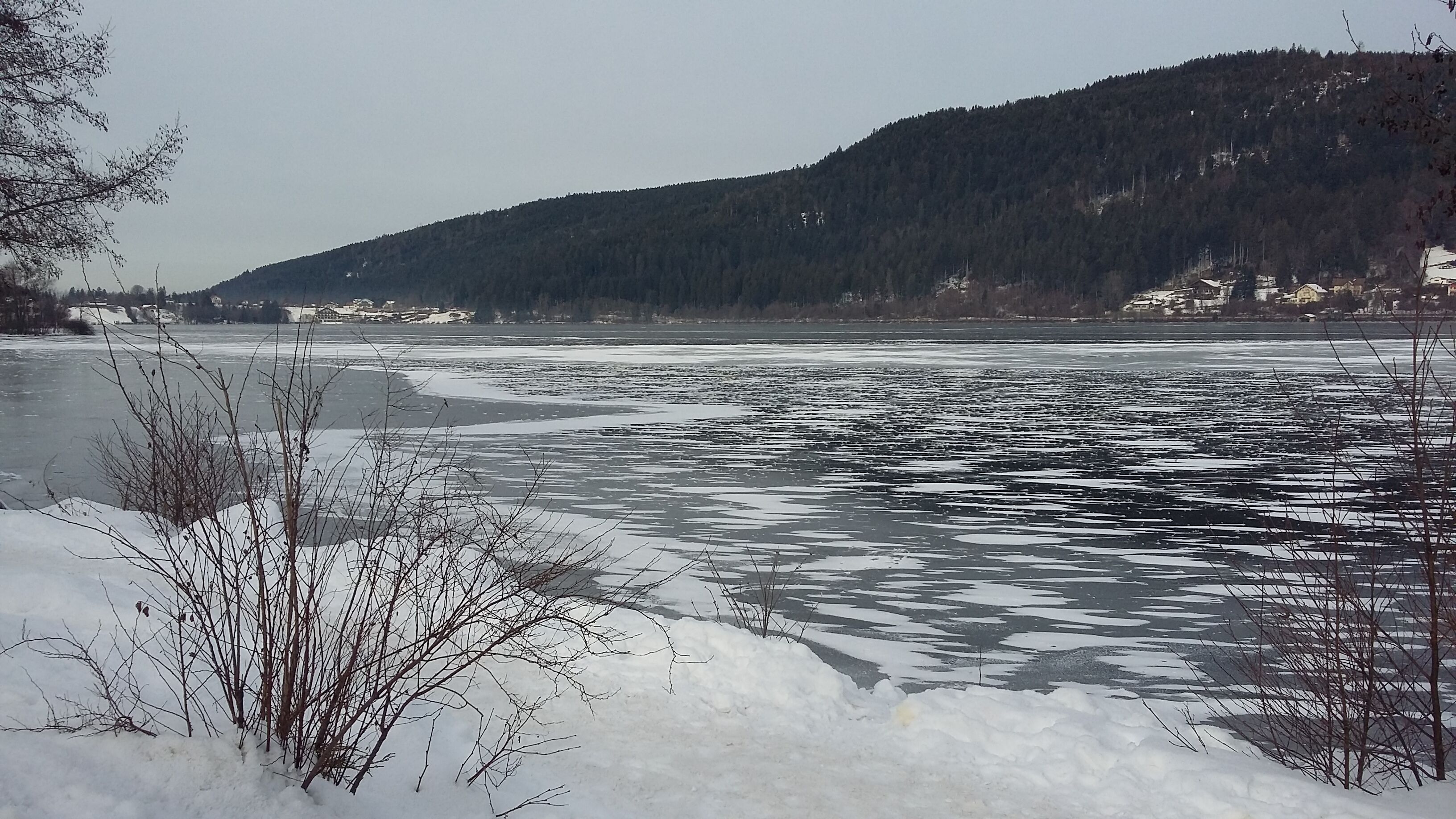 A frozen river with snow-covered banks and a forested hill in the background.