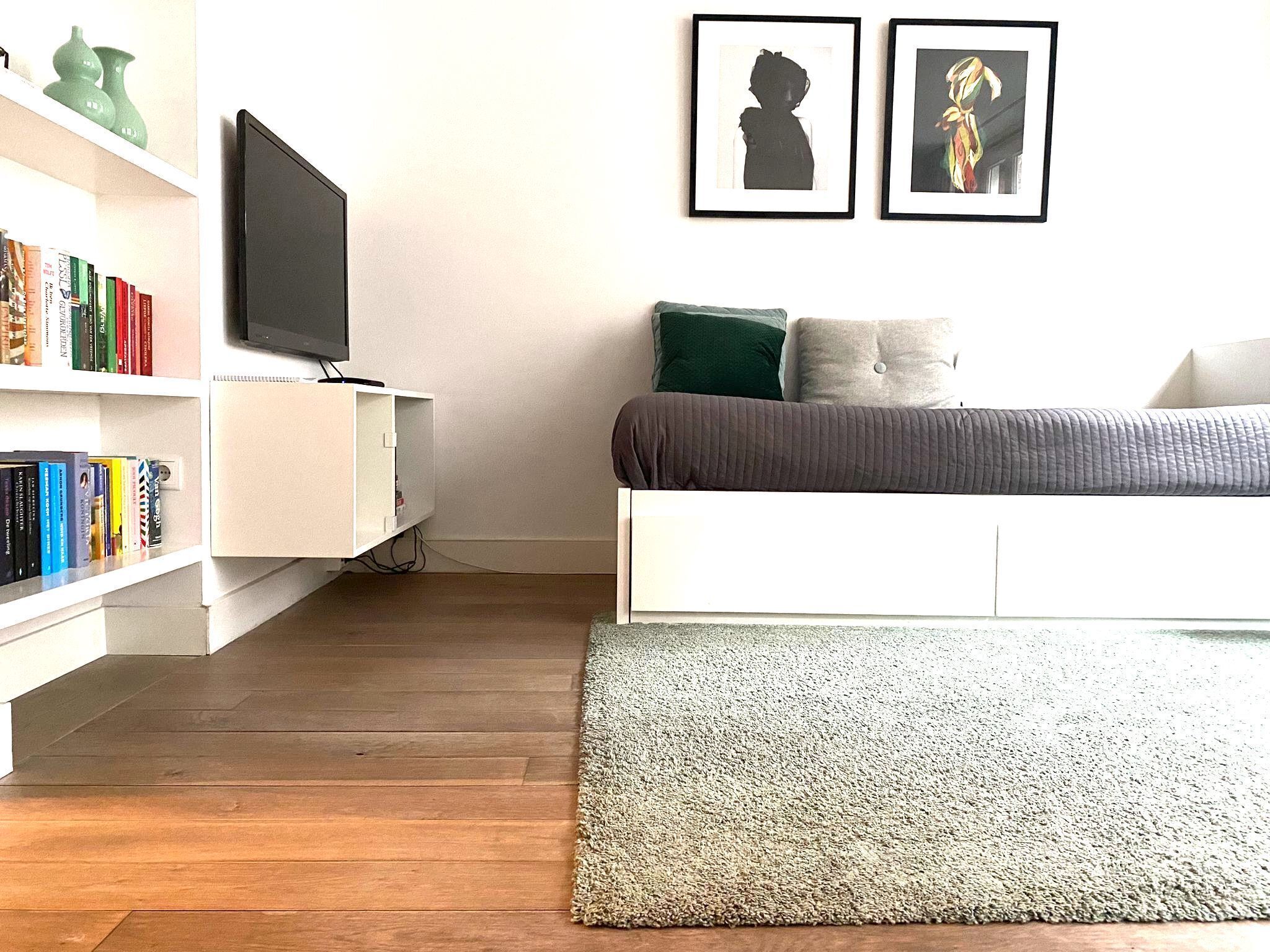 Een slaapkamer met een bed, een televisie, een boekenplank en twee ingelijste foto's aan de muur.