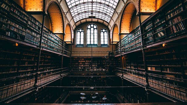 L’intérieur d’une bibliothèque, avec de hauts plafonds en arc de cercle, de grandes fenêtres et des étagères remplies de livres.
