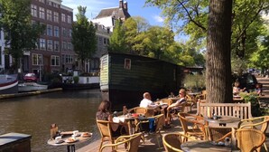 Un café situé au bord de la rivière, avec une terrasse, une structure en forme de bateau en bois et des bâtiments le long du canal.