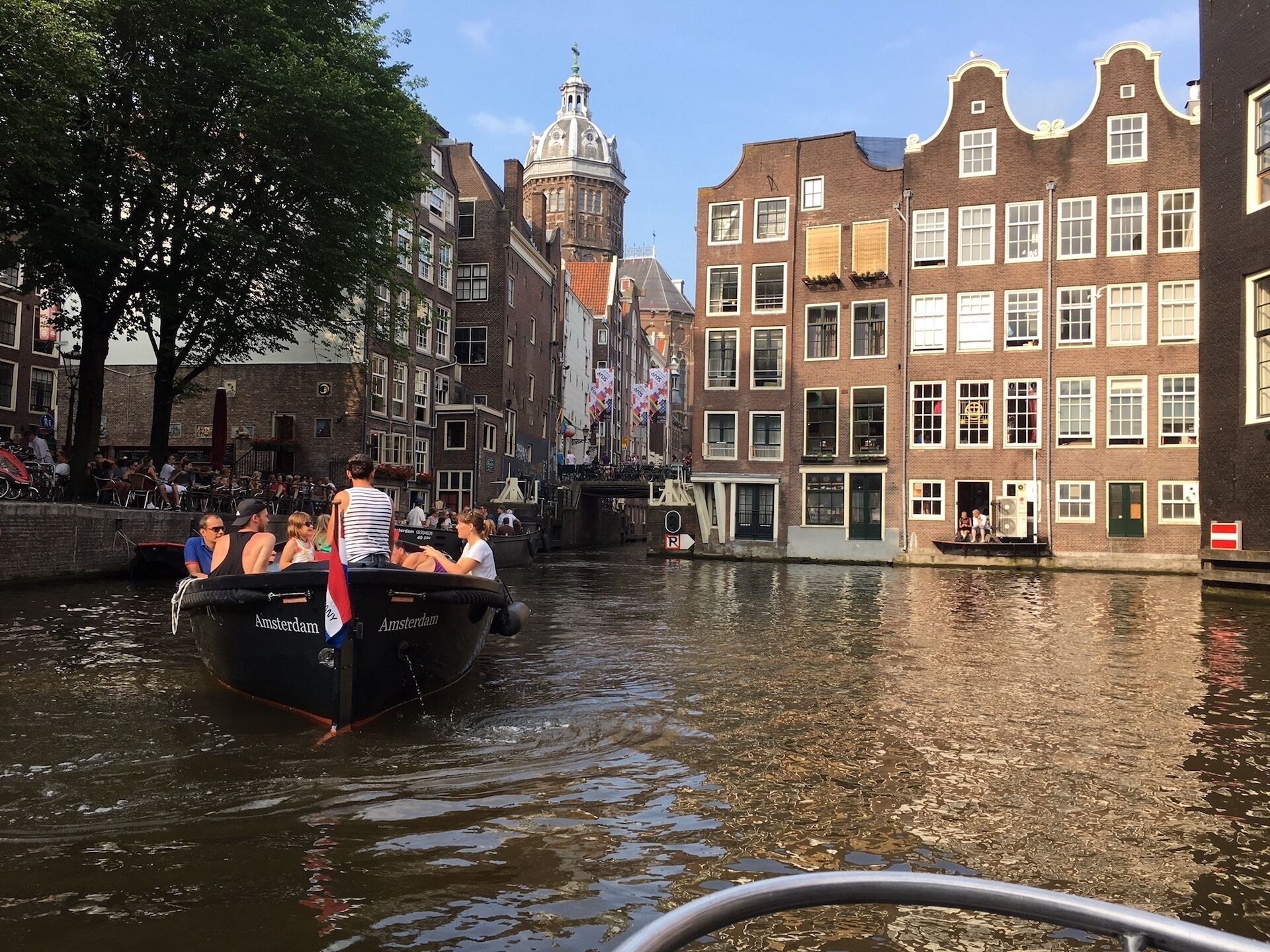 A canal boat with passengers, surrounded by historic buildings and a prominent church tower.