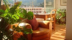 Una habitación acogedora con un sofá de cuero, una silla de madera y una mesa de comedor. Hay plantas en macetas y se ve una vista de montañas por la ventana.