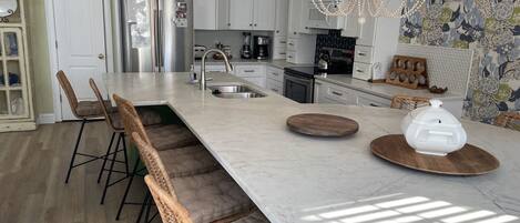 A modern kitchen with a large island, stainless steel appliances, and a chandelier.