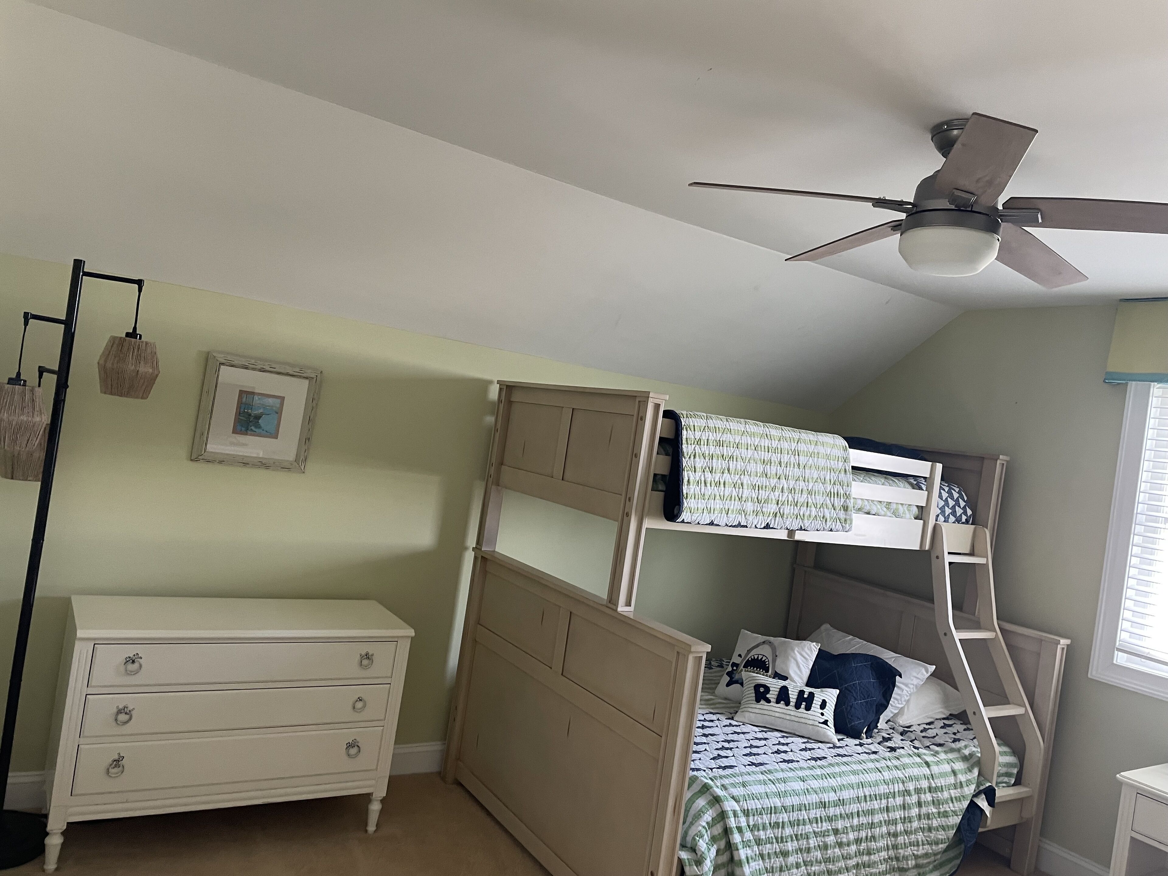 A bunk bed with a ladder, a white dresser, and a ceiling fan in a room with light green walls.