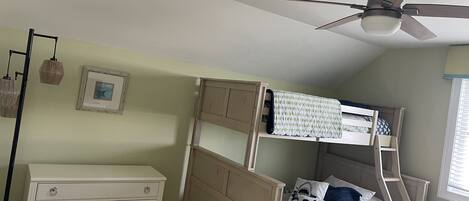 A bunk bed with a ladder, a white dresser, and a ceiling fan in a room with light green walls.