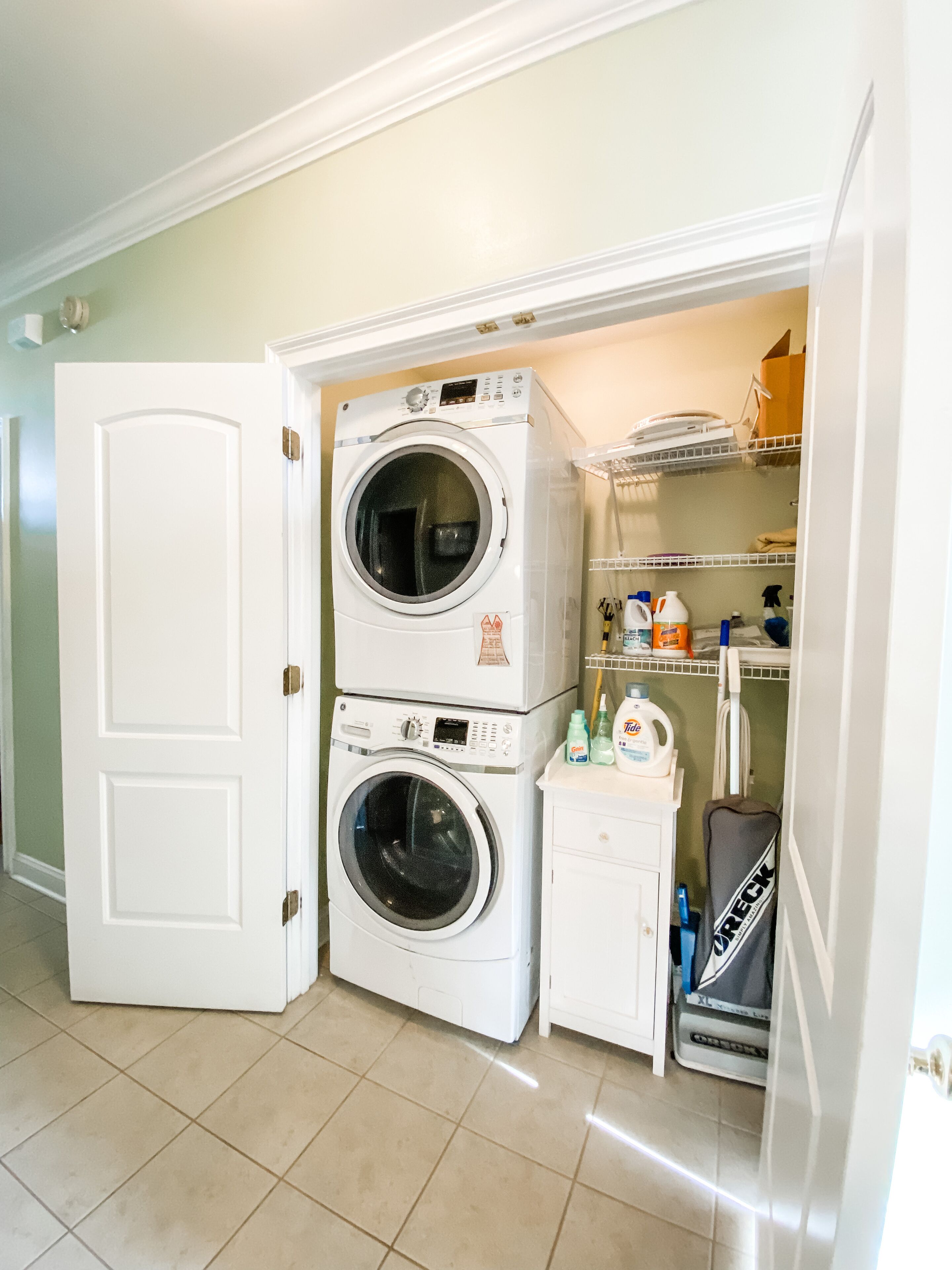 A laundry room with two stacked front-loading washing machines, a small utility cabinet, and a shoe rack.