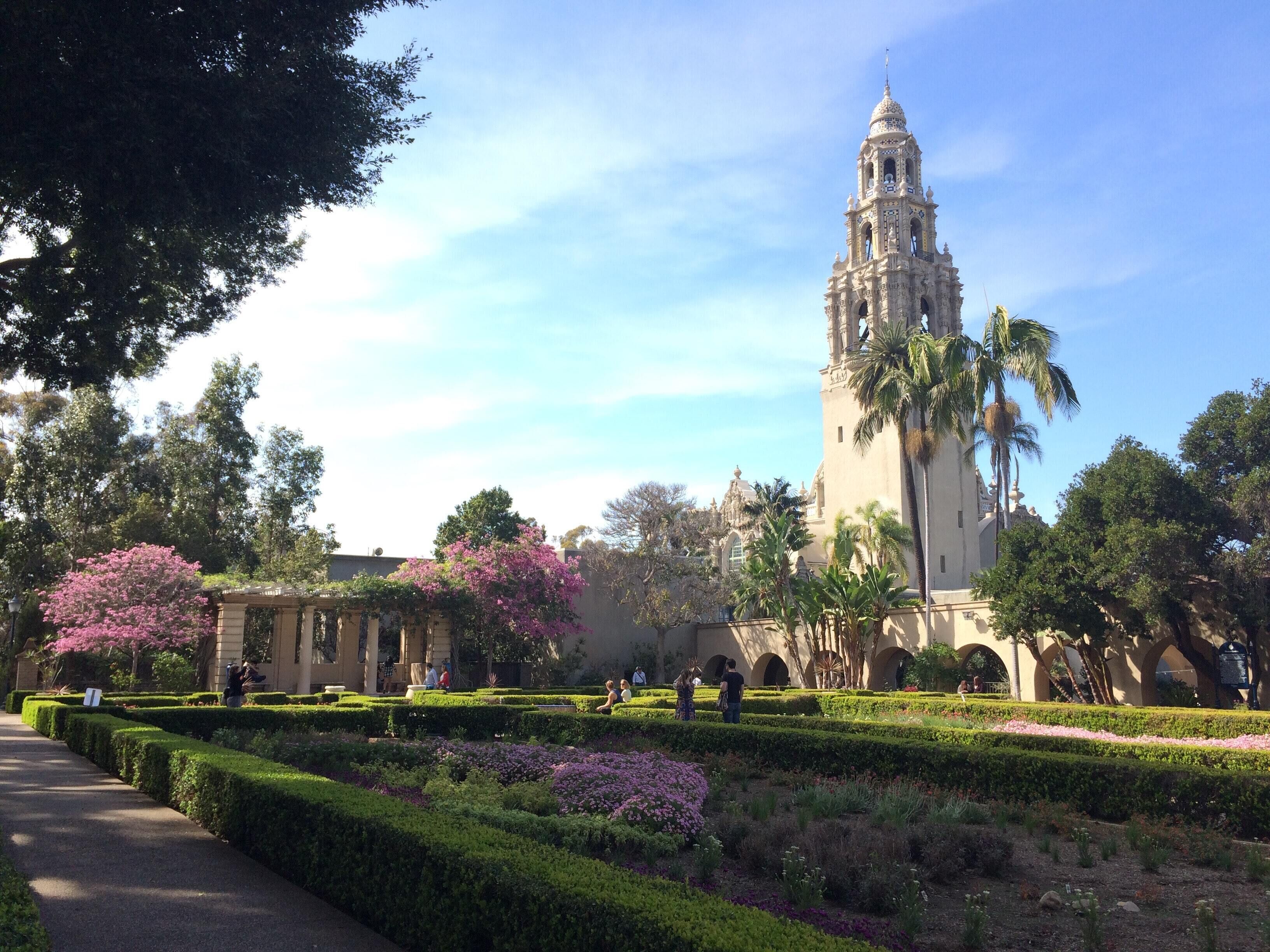 A historic building with a bell tower, surrounded by well-manicured gardens and palm trees.