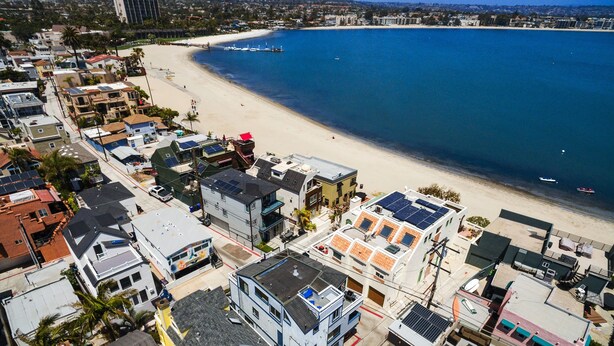 Eine Küstenwohngegend mit Strand, Häusern mit Solaranlagen und freiem Blick auf den Ozean.