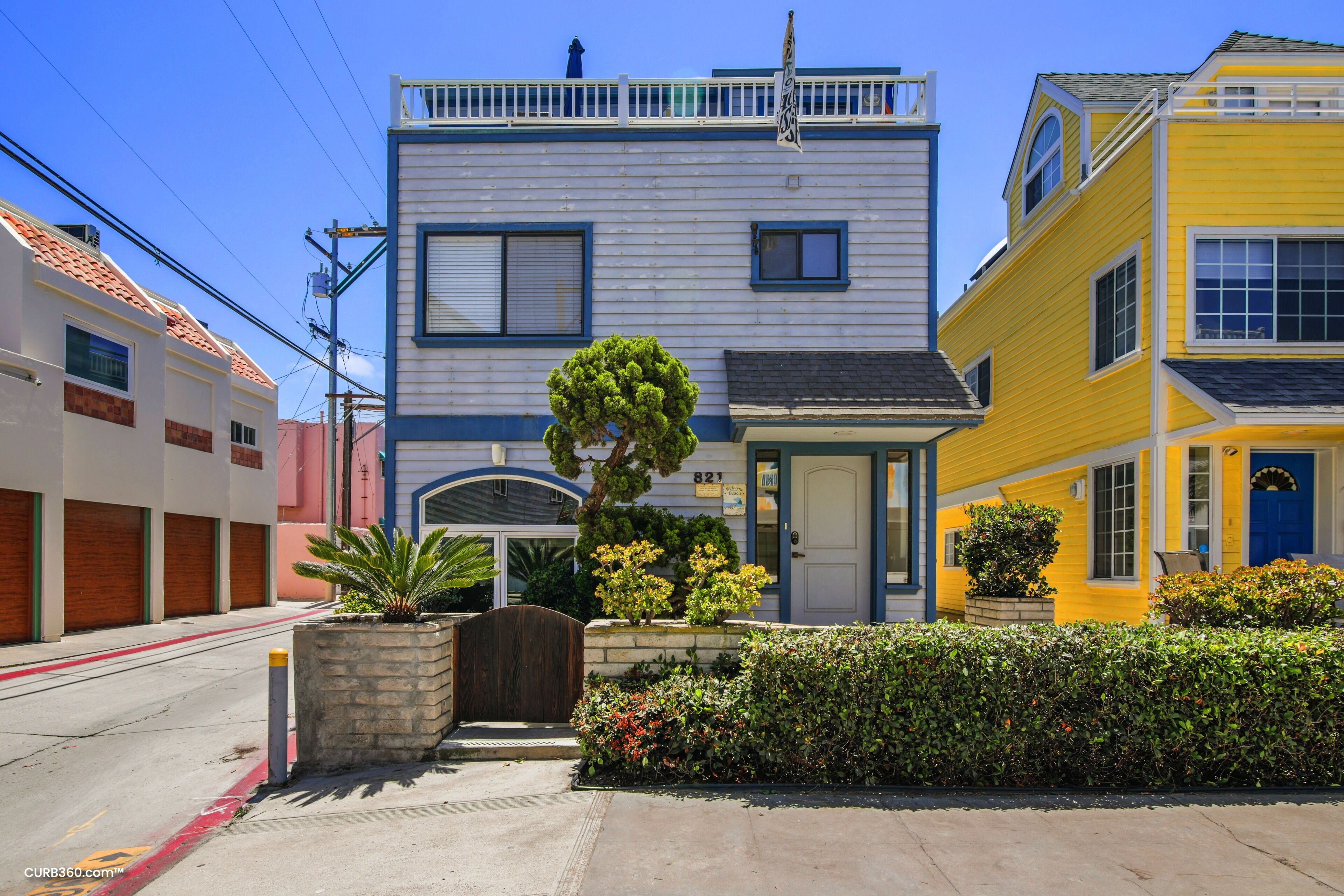 A two-story building with a blue and yellow facade, a gated entrance, and a small garden area.