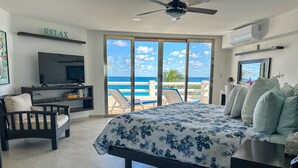 Ein Schlafzimmer mit Bett, Fernseher, Schreibtisch und Stuhl. Ein Balkon bietet Blick aufs Meer.