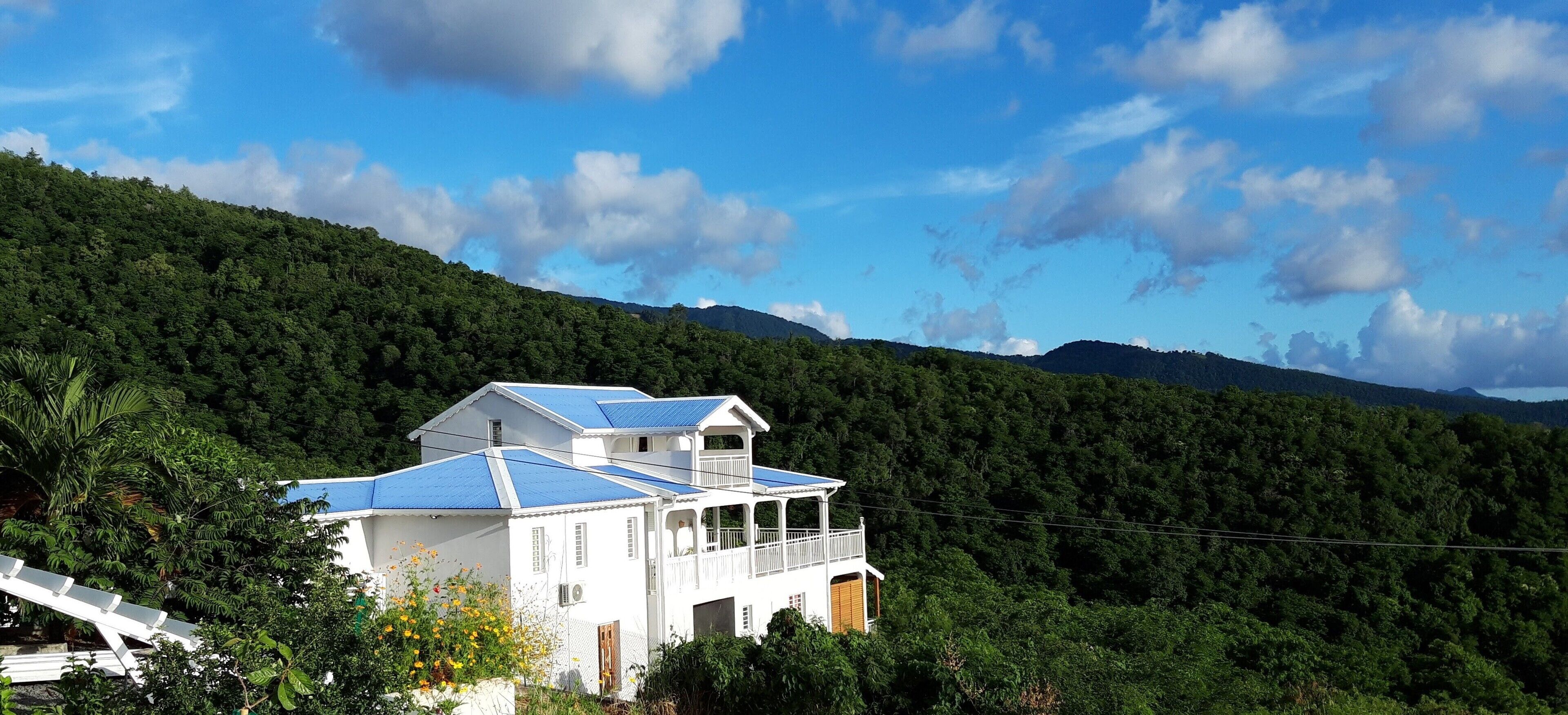 A white building with a blue roof, surrounded by lush greenery and hills.
