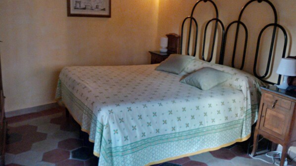 A bedroom with a bed, a nightstand, a lamp, and a wall-mounted picture.