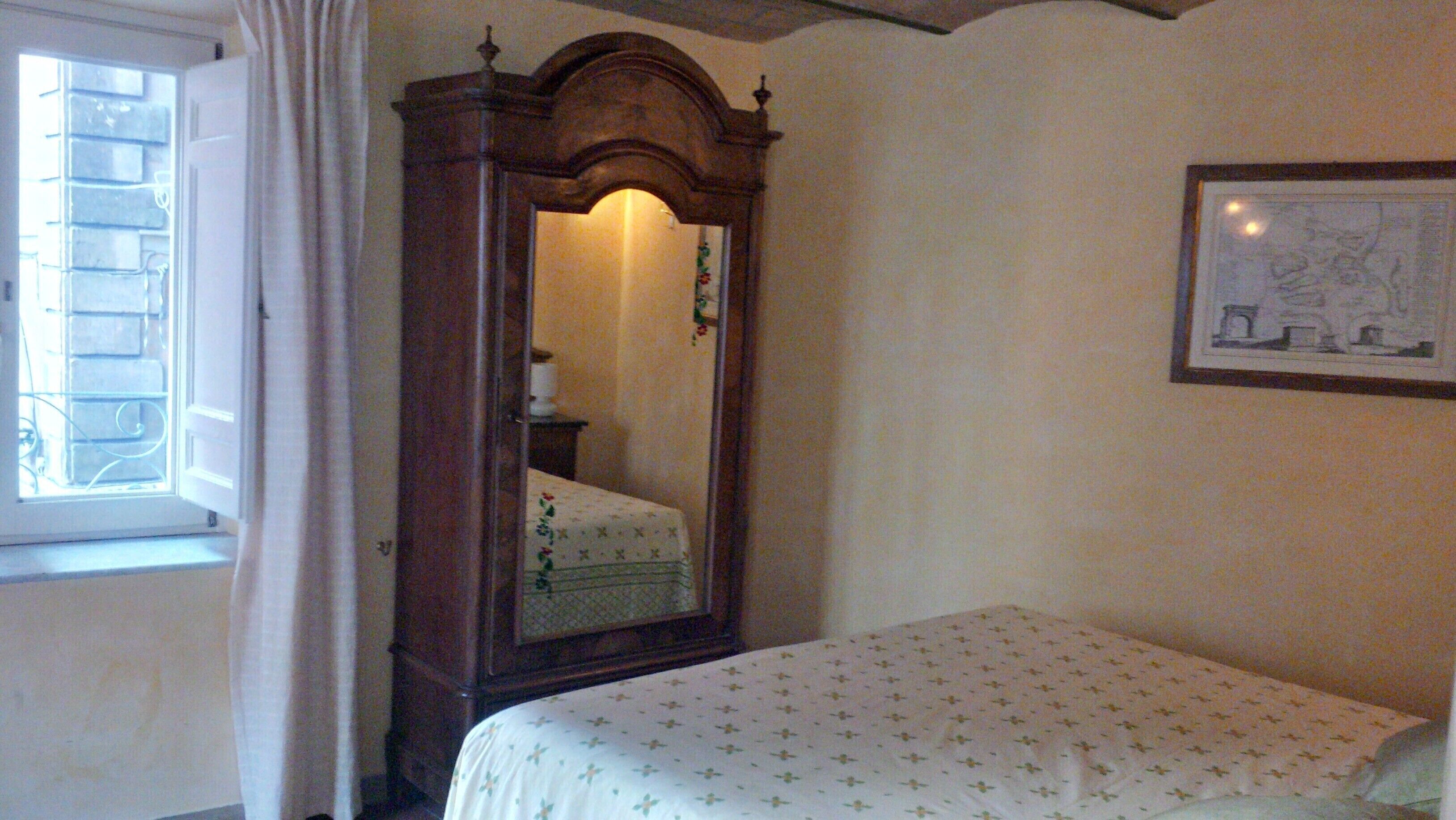 Un dormitorio con un armario de madera, una cama con colcha estampada, una ventana con cortinas y un cuadro enmarcado en la pared.