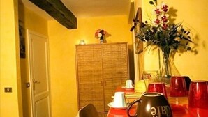 Un coin repas avec une table en bois, une nappe rouge et un vase de fleurs. Des chaises sont disposées autour de la table, et on aperçoit un buffet en bois à l’arrière-plan.