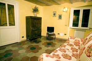A living room with a sofa, a cabinet, a television on a stand, and a window with decorative iron bars.
