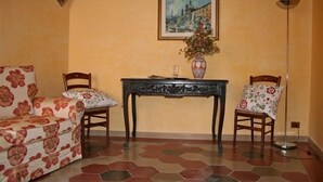Une pièce avec un canapé à motifs floraux, deux fauteuils, une table sur laquelle se trouve un vase, et un tableau accroché au mur.