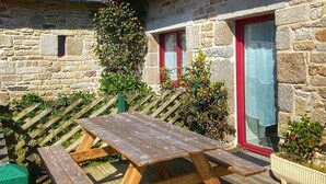 Un edificio de piedra con terraza de madera, una mesa de picnic y un pequeño jardín.