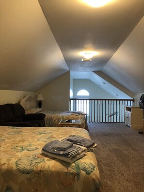 Two beds with floral-patterned bedding are situated in this room, which features a balcony with a railing offering a view of the outdoors.