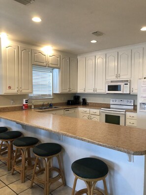 Modern kitchen with central island and bar stools, featuring a microwave, stainless steel oven, and coffee maker.