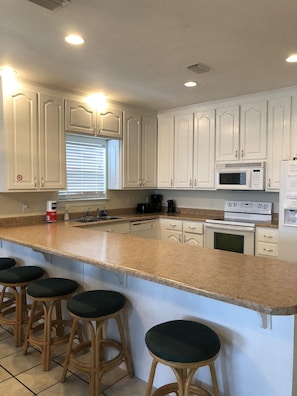 Modern kitchen with central island and bar stools, featuring a microwave, stainless steel oven, and coffee maker.