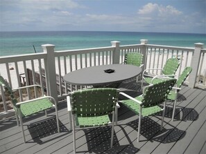 Eine Terrasse mit einem runden Tisch und grünen Stühlen mit Blick auf einen Strand.