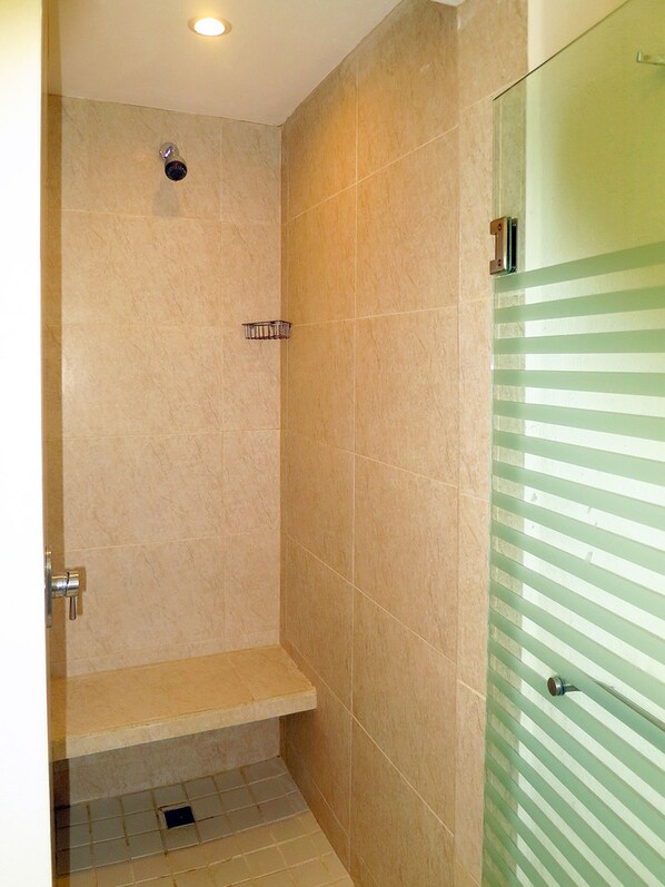 Ducha con azulejos color beige, un banco y una puerta de vidrio con franjas horizontales.