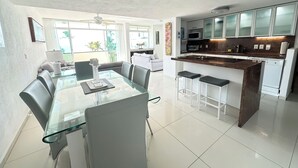 A modern kitchen with a glass dining table, white cabinets, and a built-in island with stools. - Experience the Best of Bucerias Beach Front Living (Bucerias)