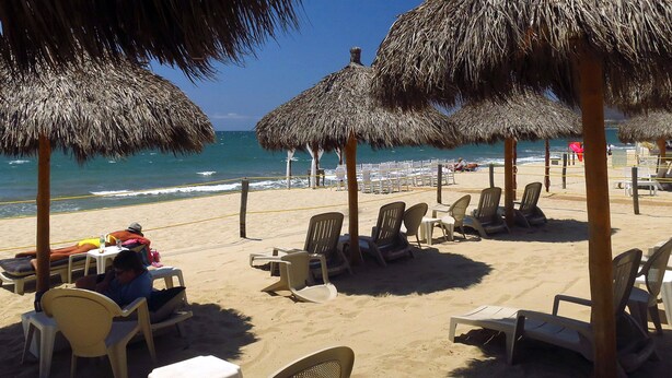 A beach with thatched umbrellas, lounge chairs, and a sandy area with a view of the ocean. - Experience the Best of Bucerias Beach Front Living (Bucerias)