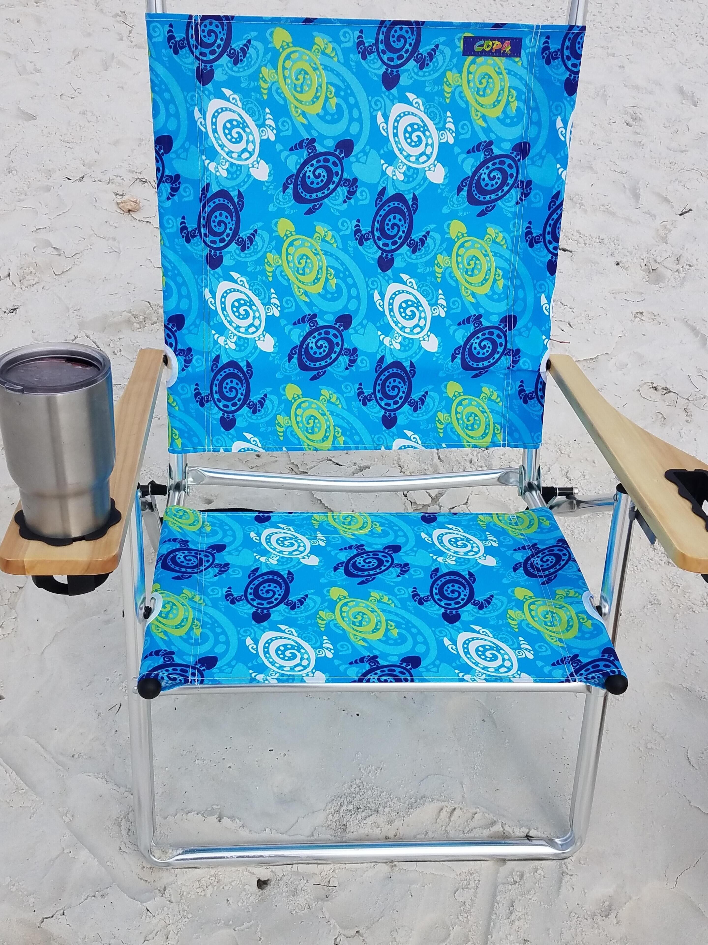 A clear glass folding chair with a vibrant blue and yellow pattern, a metal cup, and wooden armrests.