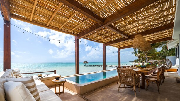 An infinity pool with a wooden deck, a sofa, and dining chairs overlooking the ocean. - LUXURY BEACHFRONT VILLA  Includes 3 Pools, Wifi, Best Snorkeling & Kayaking Bay (Tulum)
