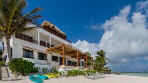 A beachfront property with a large house, a covered patio, and a sandy beach with lounge chairs. - LUXURY BEACHFRONT VILLA  Includes 3 Pools, Wifi, Best Snorkeling & Kayaking Bay (Tulum)