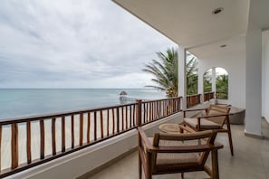 Un balcon avec vue sur l’océan, des meubles en bois et un palmier.