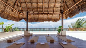 An outdoor yoga area with mats and blocks, a thatched roof, and a view of the ocean. - LUXURY BEACHFRONT VILLA  Includes 3 Pools, Wifi, Best Snorkeling & Kayaking Bay (Tulum)
