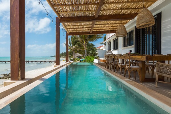 Un espace piscine doté d’une terrasse en bois, de chaises longues et offrant une vue sur l’océan.