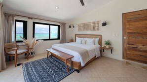 A bedroom with a large bed, a ceiling fan, a view of the sea, a wooden door, and a bench. - LUXURY BEACHFRONT VILLA  Includes 3 Pools, Wifi, Best Snorkeling & Kayaking Bay (Tulum)