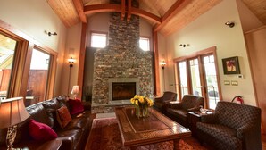 A cozy living room with a stone fireplace, wooden ceiling beams, and comfortable seating. - Exceptional Ski-in/Walk-out Home - 4100 Sft (Golden)