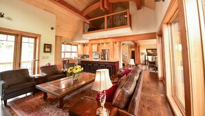 A spacious living area with a high ceiling, wooden beams, a central coffee table, sofas, and a view of the kitchen and dining area. - Exceptional Ski-in/Walk-out Home - 4100 Sft (Golden)