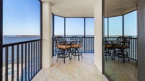 Un balcón con mesa y sillas, vista al mar y una piscina al fondo.
