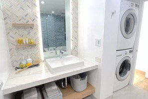 A modern bathroom with a double sink, a mirror, a washing machine, and a herringbone-patterned wall.