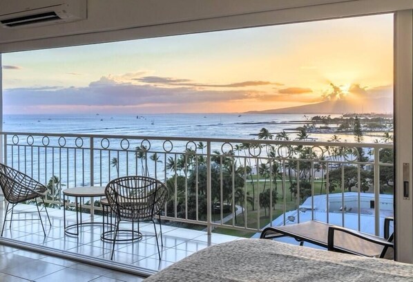 A balcony with a view of the ocean and sunset, featuring wicker chairs and a table.
