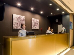 A reception desk with two staff members, a laptop, and a clock on the wall.