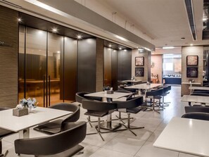 A modern dining area with multiple tables and chairs, a wooden accent wall, and a view into another room.