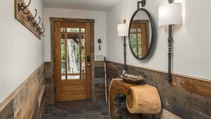 A wooden door with glass panels, a wall-mounted mirror, and a wooden bowl on a curved wooden structure.