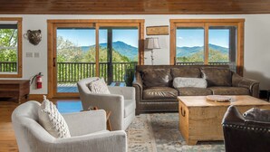 A living room with a wooden ceiling, a brown leather sofa, a white armchair, and a wooden coffee table.
