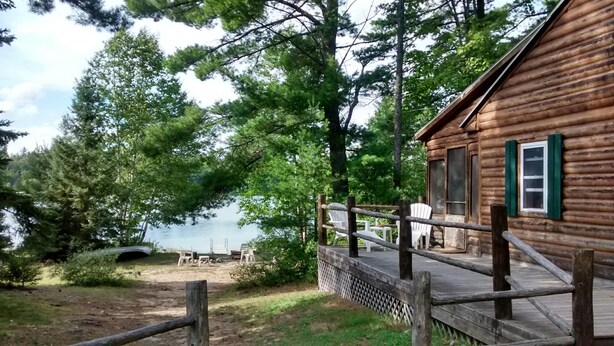 Une cabane en bois dotée d’une terrasse et offrant une vue sur un lac entouré d’arbres.